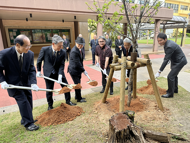 記念植樹をする城間校友会副会長、金城校友会副会長、友利校友会会長、安里副学長、鵜池常務理事、伊佐事務局長(写真左から)